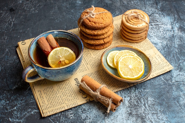 Vista lateral de la hora del té con deliciosas galletas apiladas canela limón en un periódico viejo sobre fondo oscuro