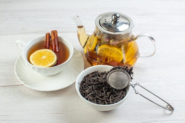 Vista lateral de la hora del té con té de hierbas mezclado con limón en una taza y una olla en la mesa blanca