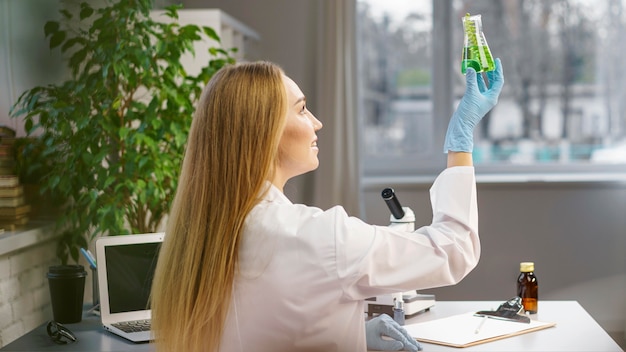 Vista lateral de la investigadora con guantes en el laboratorio con tubo de ensayo