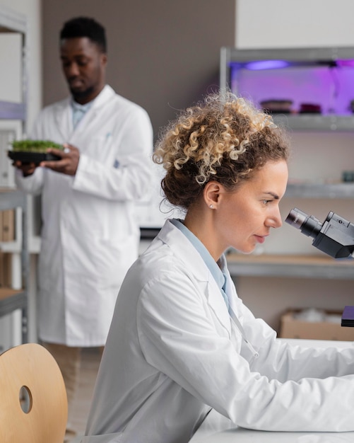 Vista lateral de la investigadora en el laboratorio con microscopio y colega masculino