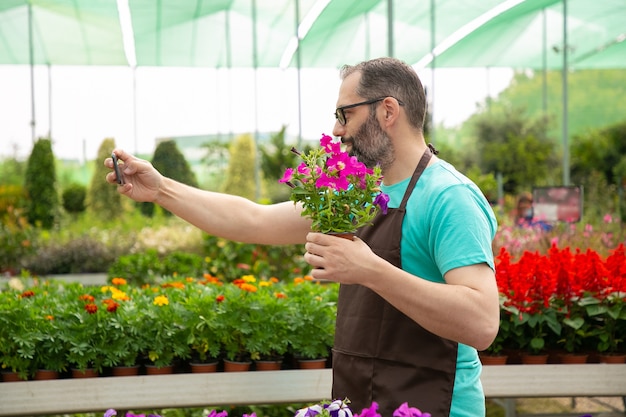 Foto gratuita vista lateral del jardinero canoso tomando selfie con petunia