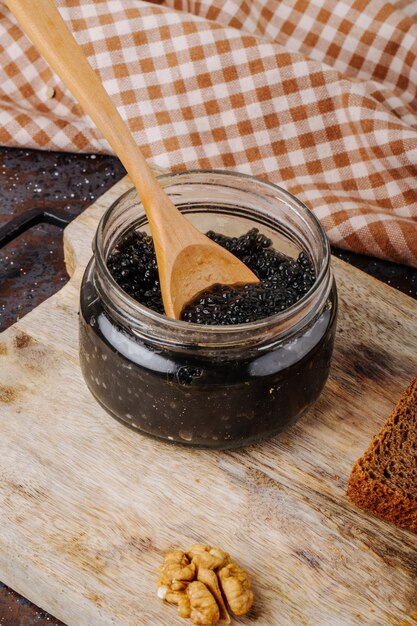 Vista lateral jarra de caviar negro con superficie de madera pan de centeno y nueces en un tablero