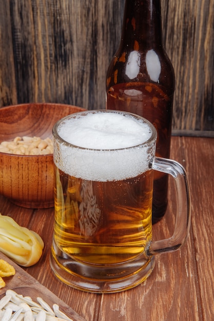 Vista lateral de una jarra de cerveza con maní salado en un tazón de madera en rústico