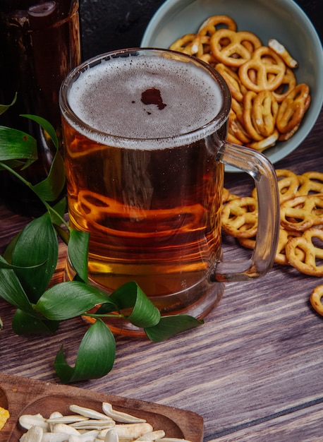 Vista lateral de una jarra de cerveza con mini pretzels en rústico