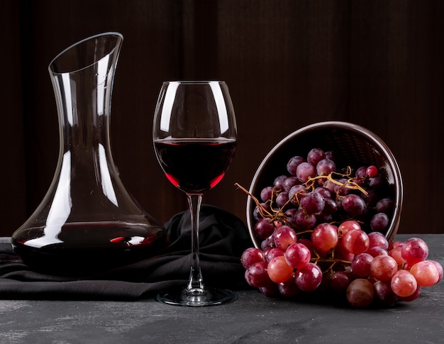 Vista lateral de la jarra con vino tinto y uva en horizontal oscuro
