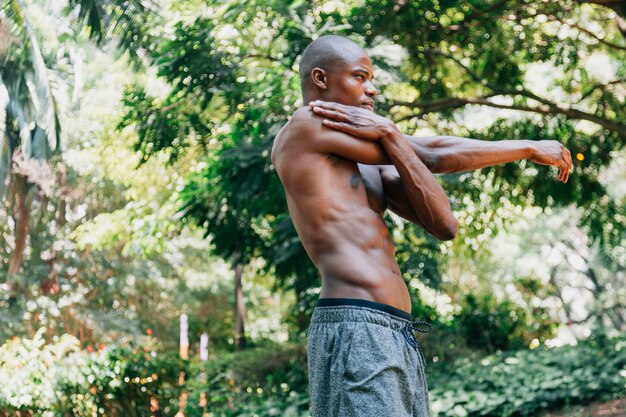 Vista lateral de un joven africano haciendo ejercicios de estiramiento en el parque