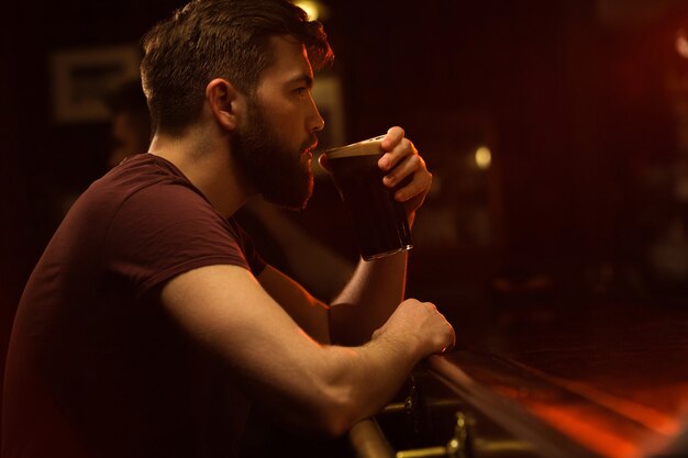 Vista lateral de un joven bebiendo un vaso de cerveza