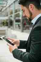 Foto gratuita vista lateral de un joven empresario guapo usando un teléfono inteligente contra telón de fondo borroso