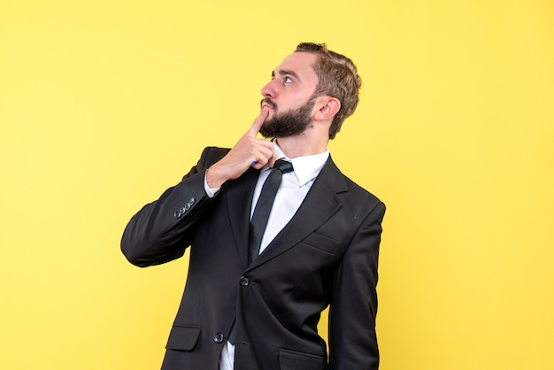 Vista lateral del joven empresario pensativo presionando su dedo acusador sobre la barbilla en la pared amarilla