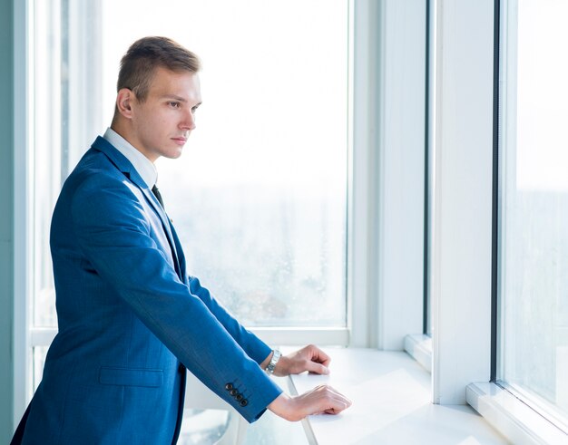 Vista lateral de un joven empresario de pie junto a la ventana en la oficina