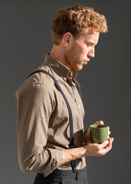 Vista lateral joven modelo masculino sosteniendo una taza de café