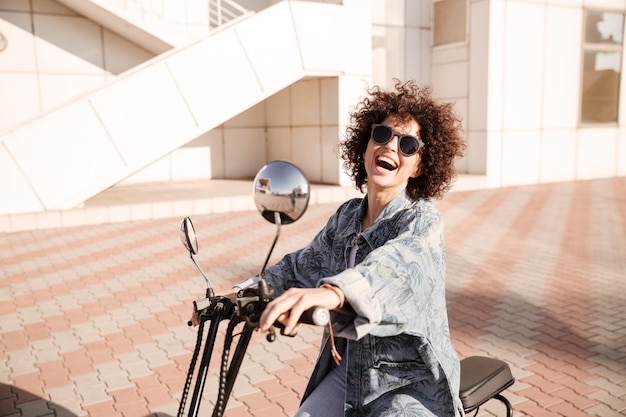 Foto gratuita vista lateral de la joven mujer rizada alegre en gafas de sol posando