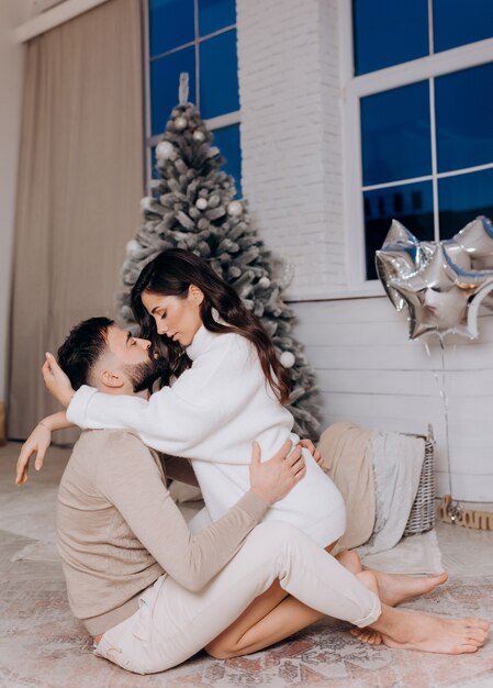 Vista lateral de la joven pareja abrazándose y disfrutando del momento cerca del árbol de Navidad