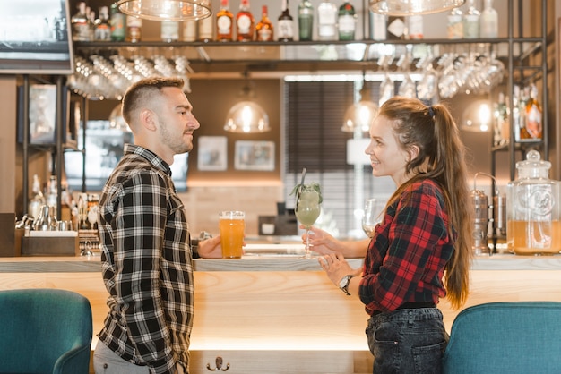 Vista lateral de la joven pareja de pie cerca de la barra de bar mirando el uno al otro