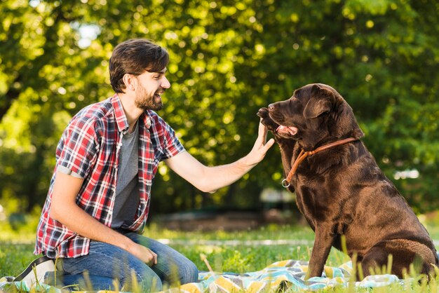 Vista lateral de un joven sonriente divirtiéndose con su perro en el jardín