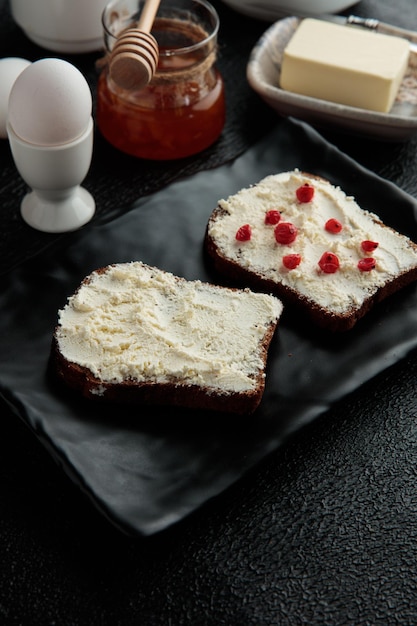 Foto gratuita vista lateral del juego de desayuno con requesón untado en rebanadas de pan con grosella roja y mantequilla de mermelada de membrillo de huevos sobre fondo negro