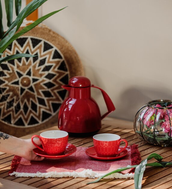 Vista lateral del juego de té rojo de tazas y tetera en una mesa de madera