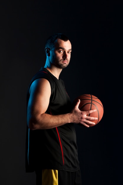 Vista lateral del jugador de baloncesto posando mientras sostiene la pelota