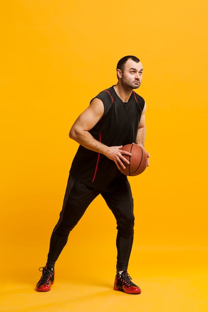 Vista lateral del jugador masculino posando con baloncesto