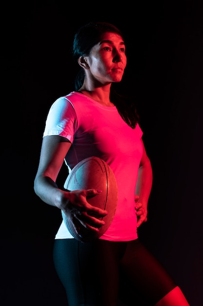 Vista lateral del jugador de rugby femenino atlético sosteniendo la bola