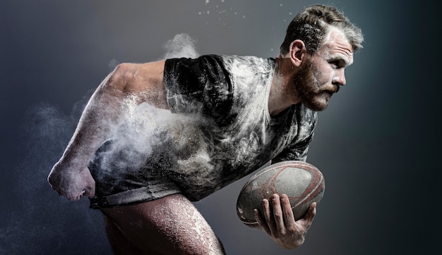 Vista lateral del jugador de rugby masculino atlético sosteniendo la bola con polvo