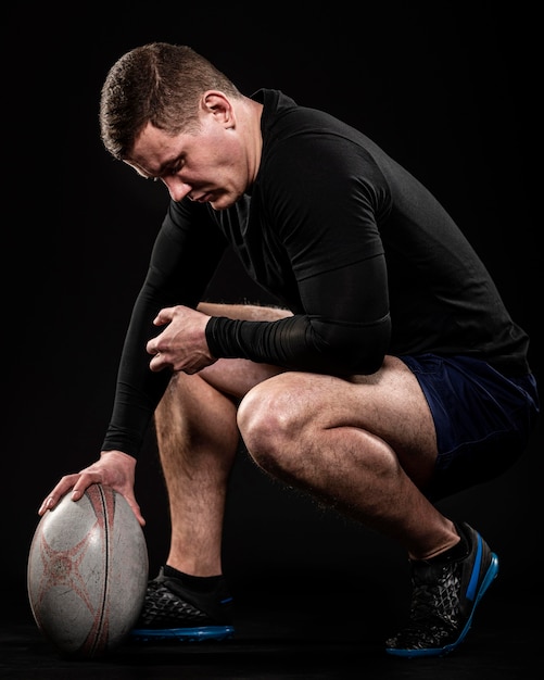 Vista lateral del jugador de rugby masculino sosteniendo la pelota con una mano