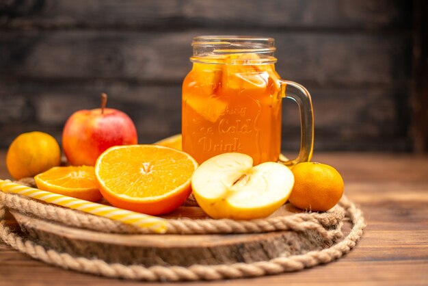 Vista lateral de jugo fresco orgánico en una botella servida con tubo y frutas sobre una tabla de cortar y sobre una mesa de madera marrón