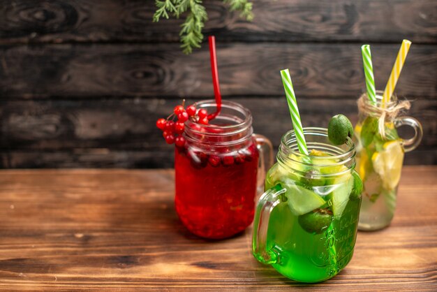 Vista lateral de jugos frescos orgánicos en botellas servidas con tubos y frutas en el lado izquierdo sobre una mesa marrón