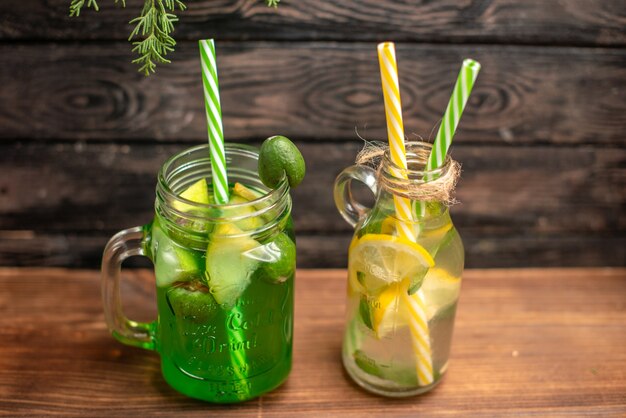 Vista lateral de jugos frescos orgánicos en botellas servidas con tubos y frutas sobre una mesa marrón