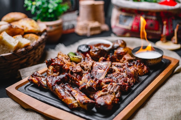 Vista lateral kebab de carne con papas a la parrilla y verduras con salsa y fuego en un tablero