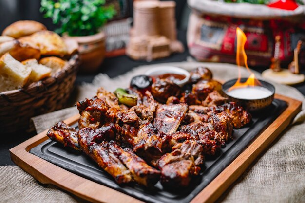 Vista lateral kebab de carne con papas a la parrilla y verduras con salsa y fuego en un tablero