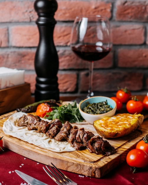 Vista lateral del kebab de cordero con hierbas y verduras sobre una plancha de madera