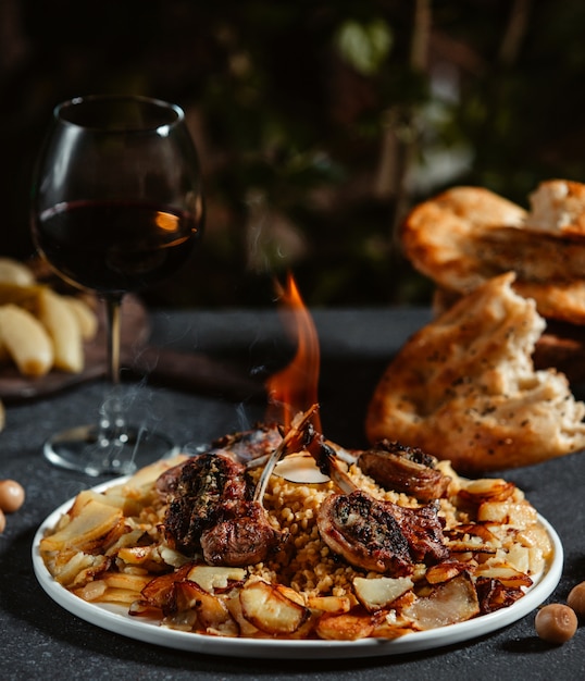 Vista lateral de kebab de costillas de cordero con patatas fritas en una mesa negra