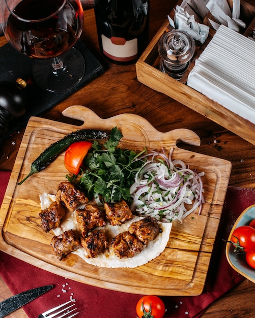 Vista lateral del kebab de pollo con cebolla y hierbas sobre una tabla de madera