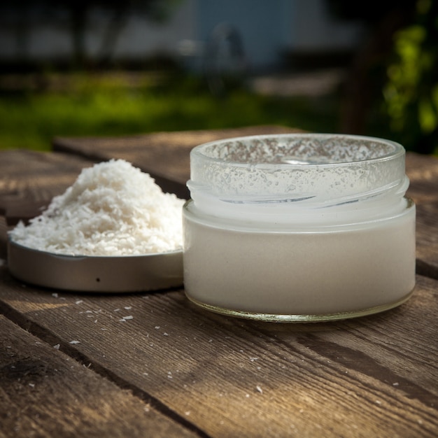 Vista lateral de leche de coco con tarro y migas de coco y tapa en mesa de madera