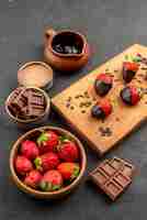 Foto gratuita vista lateral desde lejos fresas a bordo de crema de chocolate y fresas y fresas cubiertas de chocolate en la tabla de cortar de la cocina en la mesa oscura