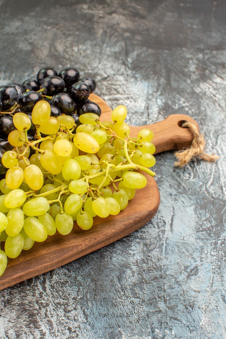 Foto gratuito vista lateral desde lejos tabla de cortar de madera de uvas con las apetitosas uvas verdes y negras