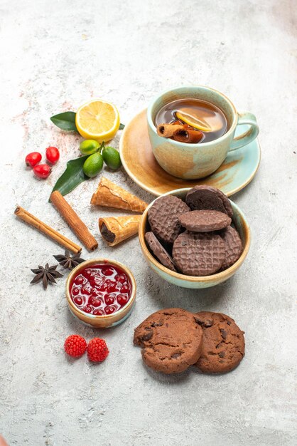 Vista lateral desde lejos una taza de té una taza de té galletas de chocolate bayas palitos de canela mermelada de limas