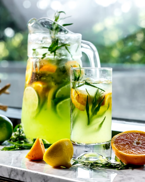 Vista lateral limonada vigorizante con limón, lima, naranja y estragón