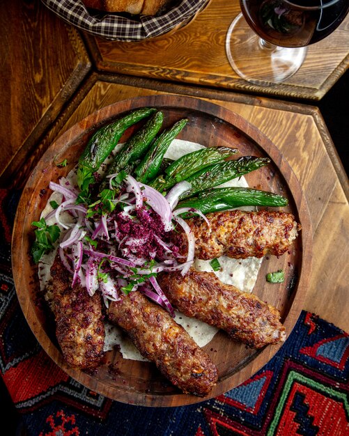 Vista lateral de lula kebab con cebolla roja sumakh y chiles verdes a la parrilla sobre una tabla de madera sobre la mesajpg