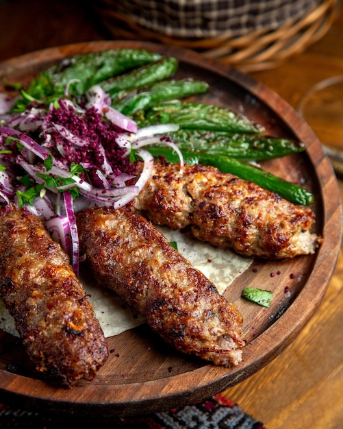 Vista lateral de lula kebab con cebolla roja sumakh y chiles verdes a la parrilla sobre una tabla de madera