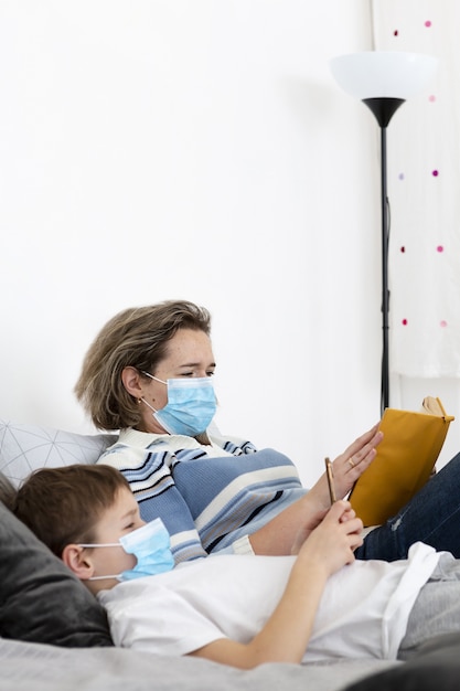 Vista lateral de la madre y el niño en la cama con máscaras médicas