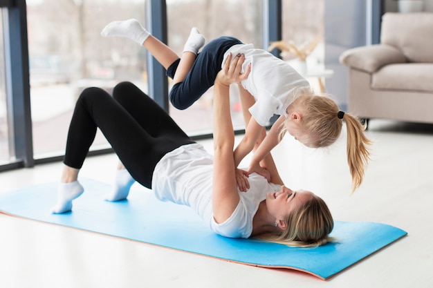 Vista lateral de la madre que levanta a la hija feliz en el aire mientras está en la estera de yoga