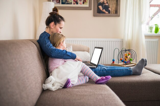 Vista lateral de una madre sentada con su hija usando una computadora portátil