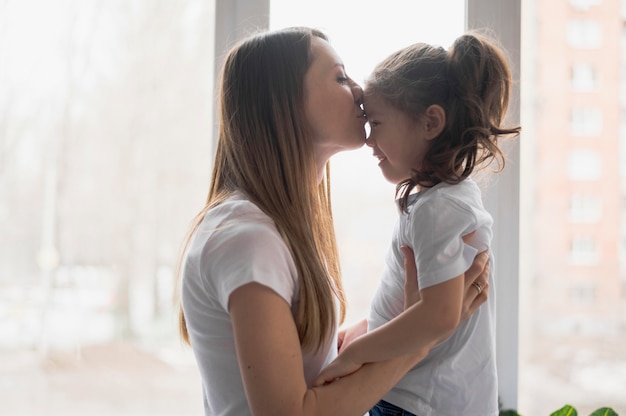 Foto gratuita vista lateral mamá besando a niña en la frente