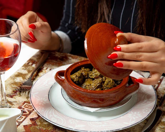 Vista lateral de manos femeninas abriendo olla de barro con hojas de uva tradicional dolma