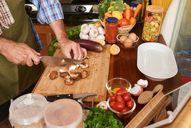 Vista lateral de manos masculinas cortando champiñones para el plato orgánico