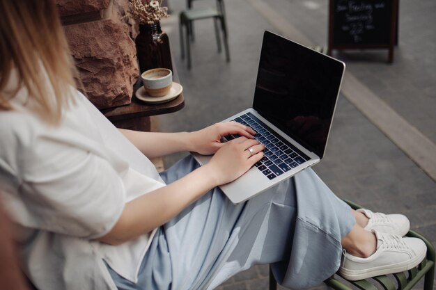La vista lateral de las manos de la mujer en la computadora portátil en el café