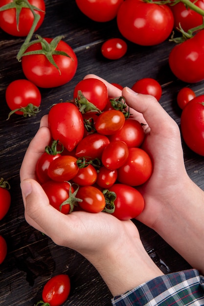 Vista lateral de manos de mujer sosteniendo tomates con otros sobre superficie de madera