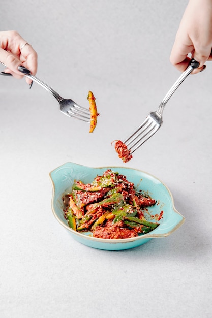 Vista lateral de manos sostenga tenedores sobre el plato con ensalada de aguacate con carne y sésamo